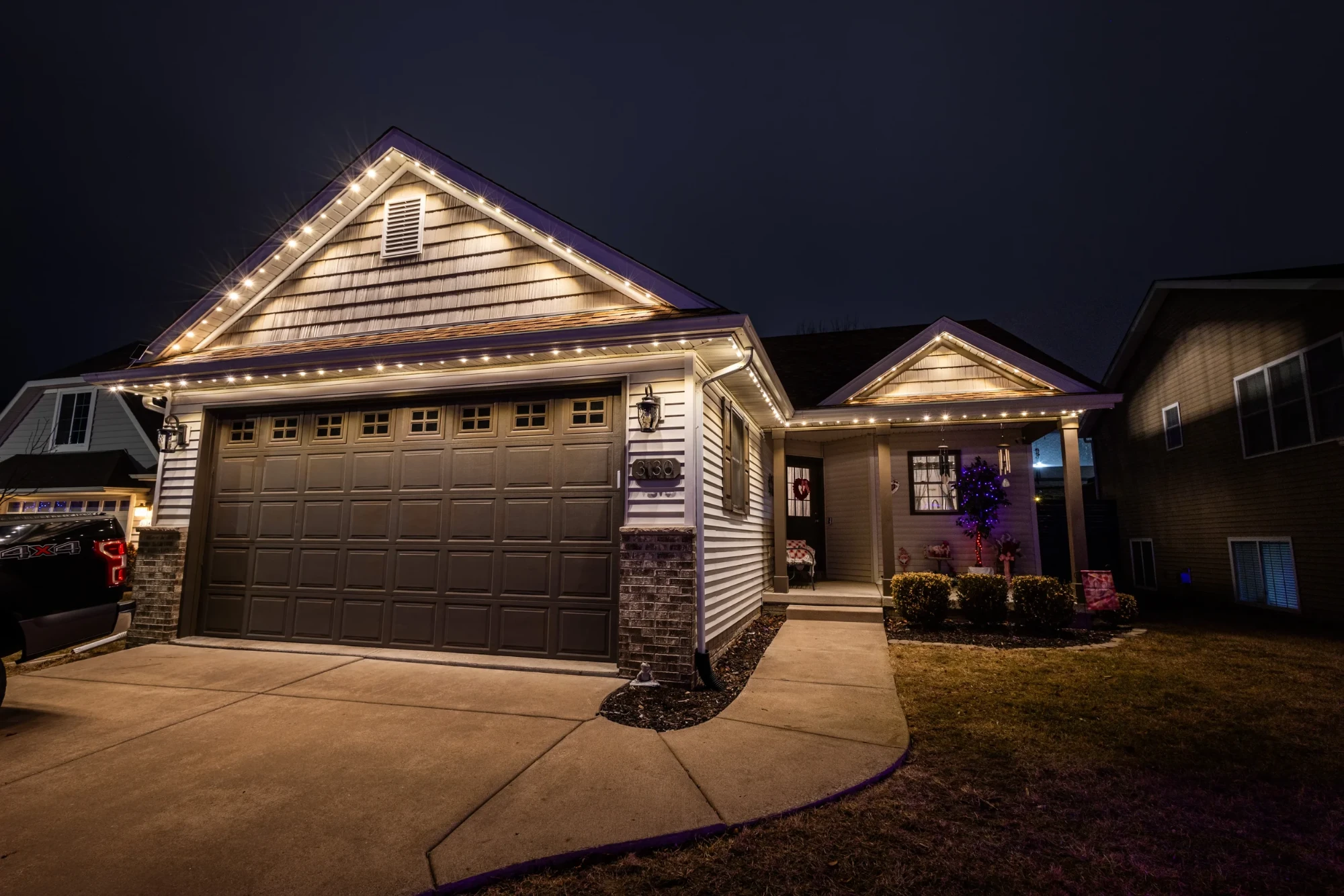 Home with warm white permanent lighting over the garage and porch
