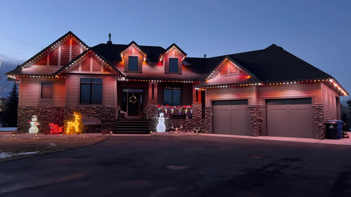 Home with warm white and red permanent lighting at dusk with holiday decor