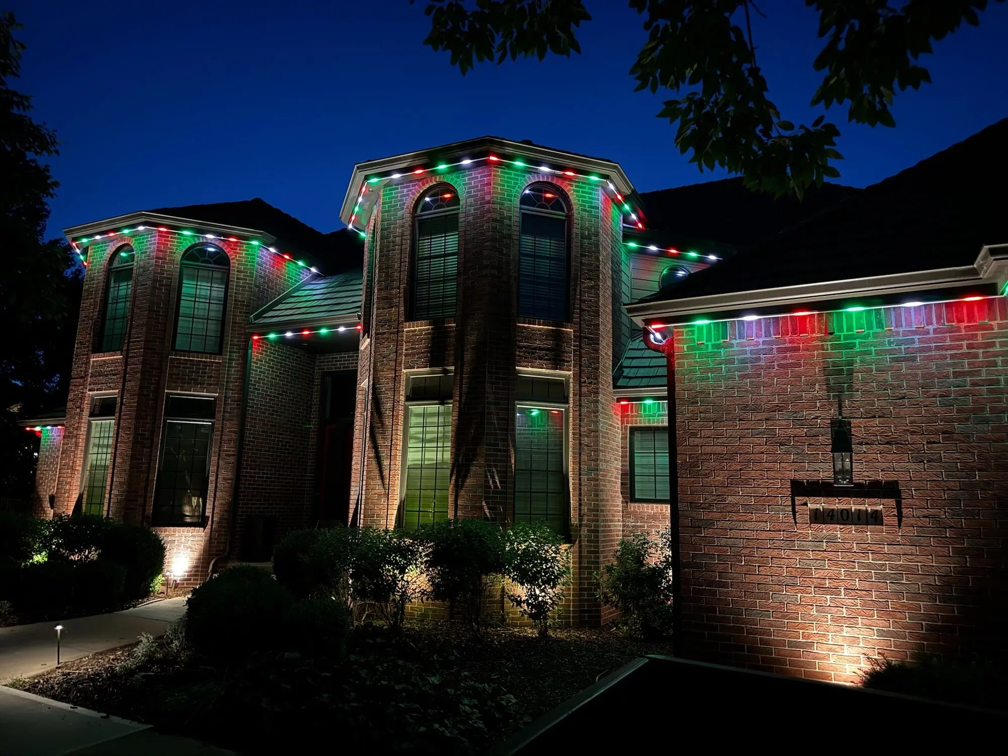 Two-story brick home with red, green and white permanent roofline lighting
