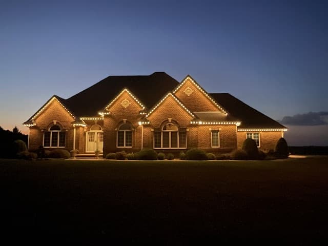 Brick ranch home with warm white permanent roofline lighting at dusk